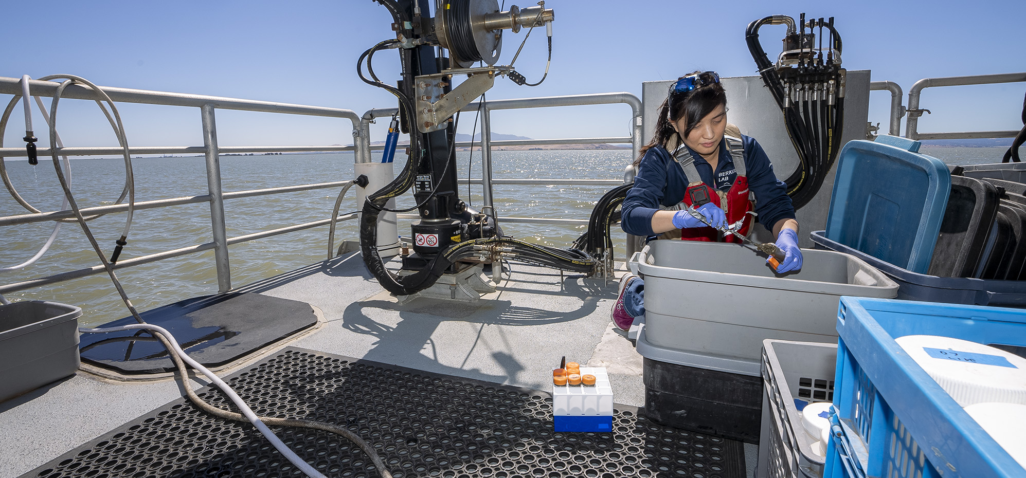 A researcher kneeling on a boat deck next to a sampling container.