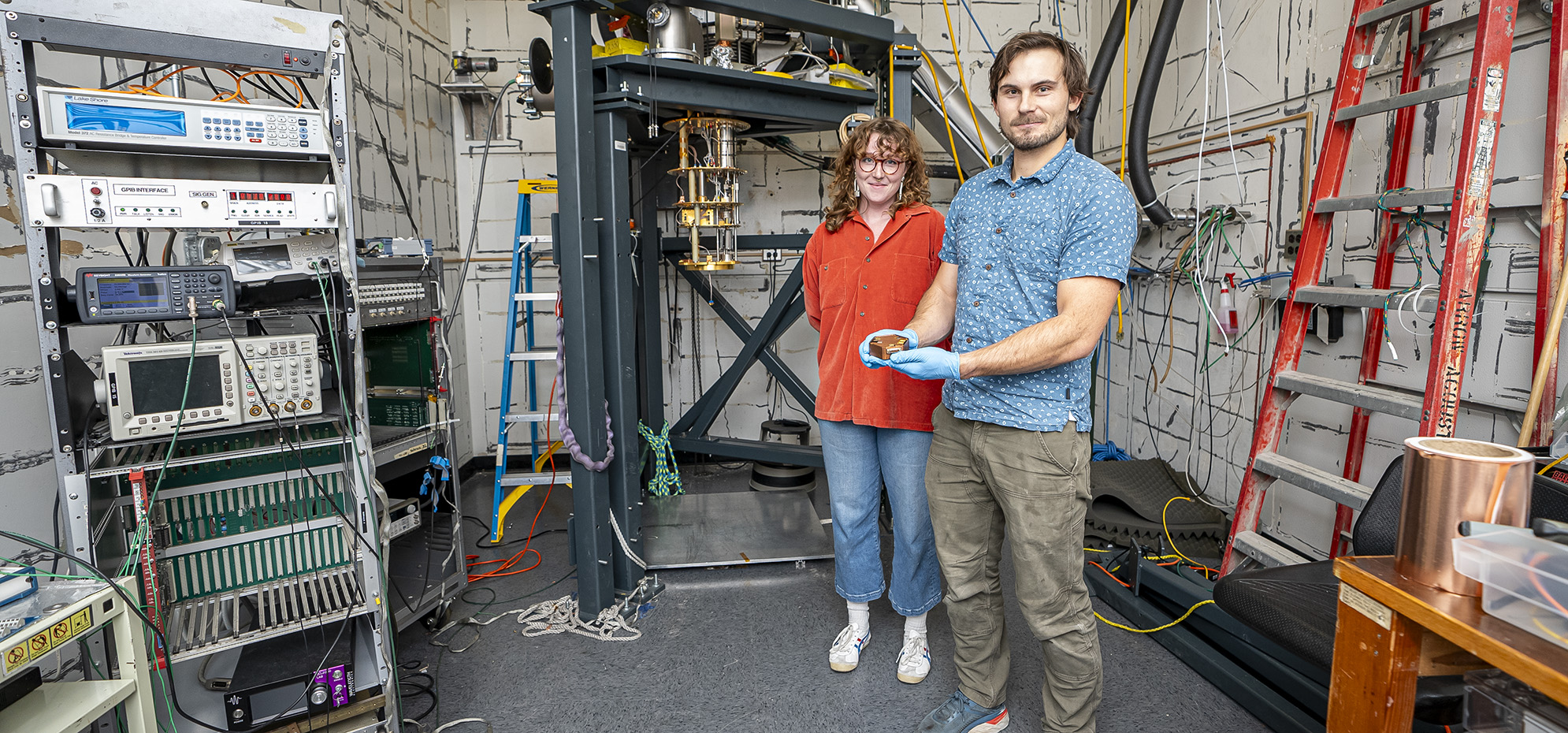 Two researchers stand in a laboratory, with one holding the TESSERACT detector with gloved hands.