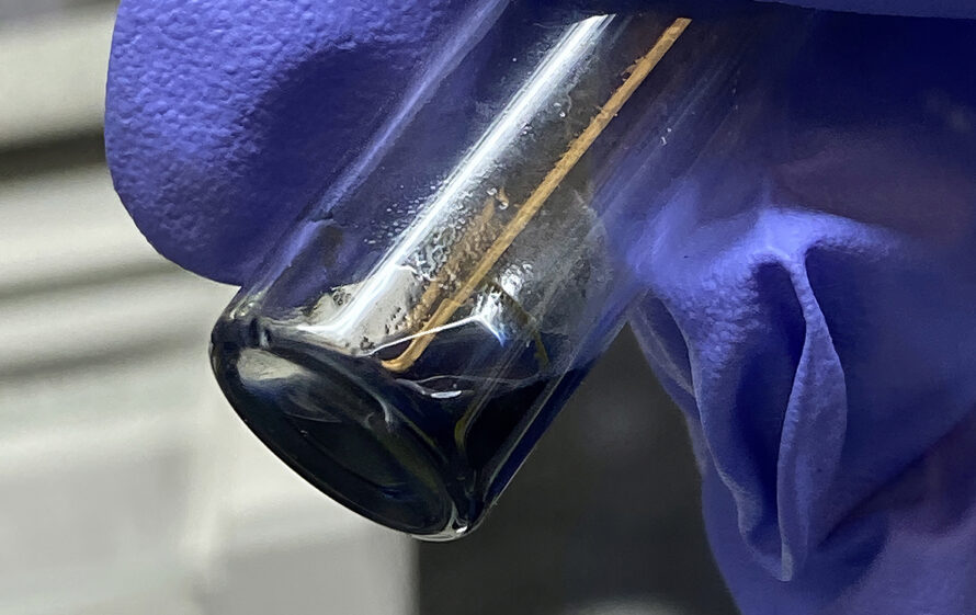 A purple gloved hand holding a small vial with dark blue liquid.